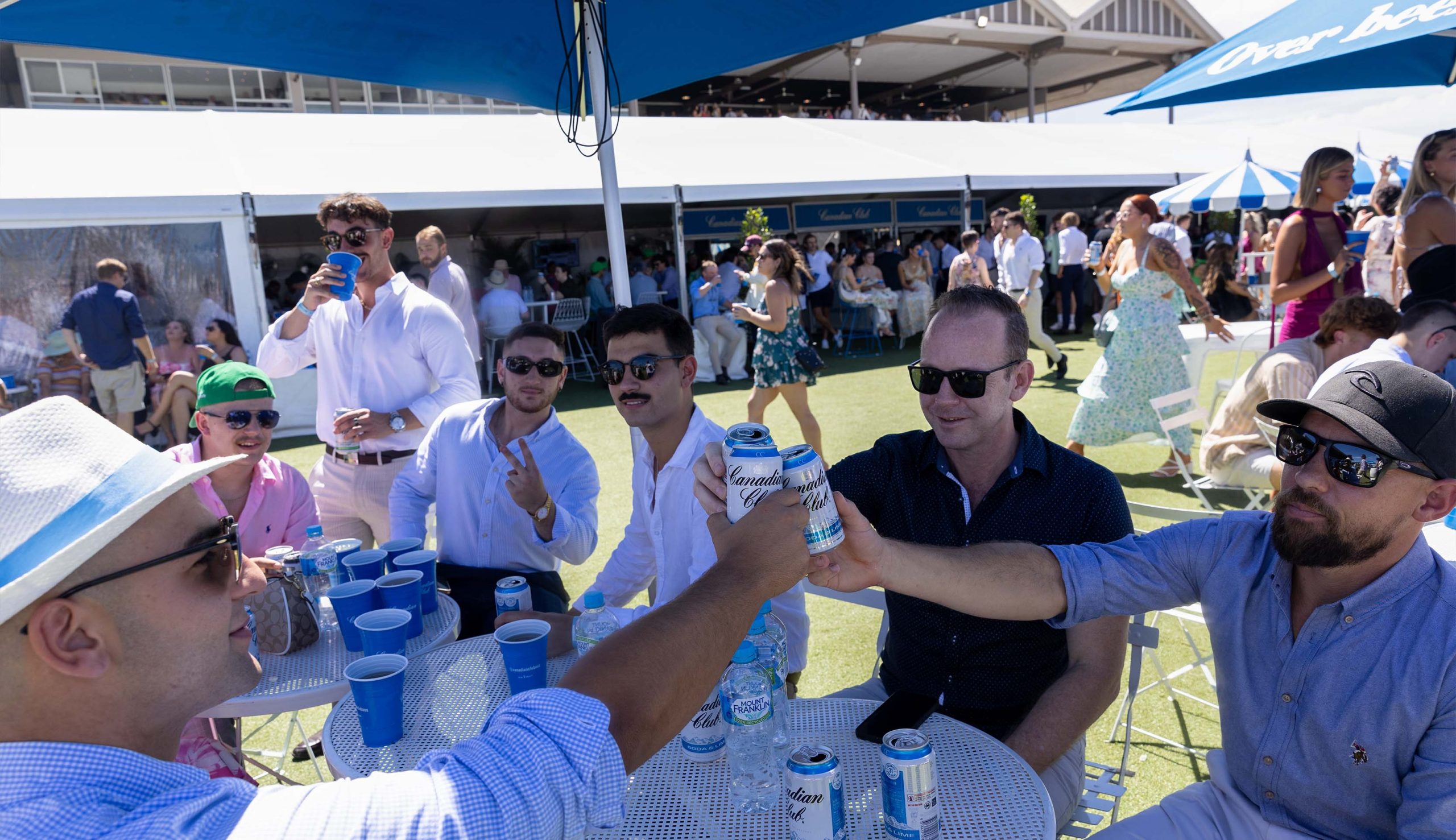 group of three men cheers cans together in canadian club marquee